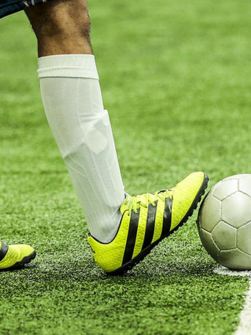 A man withbright yellow football boots rests his foot on a ball.