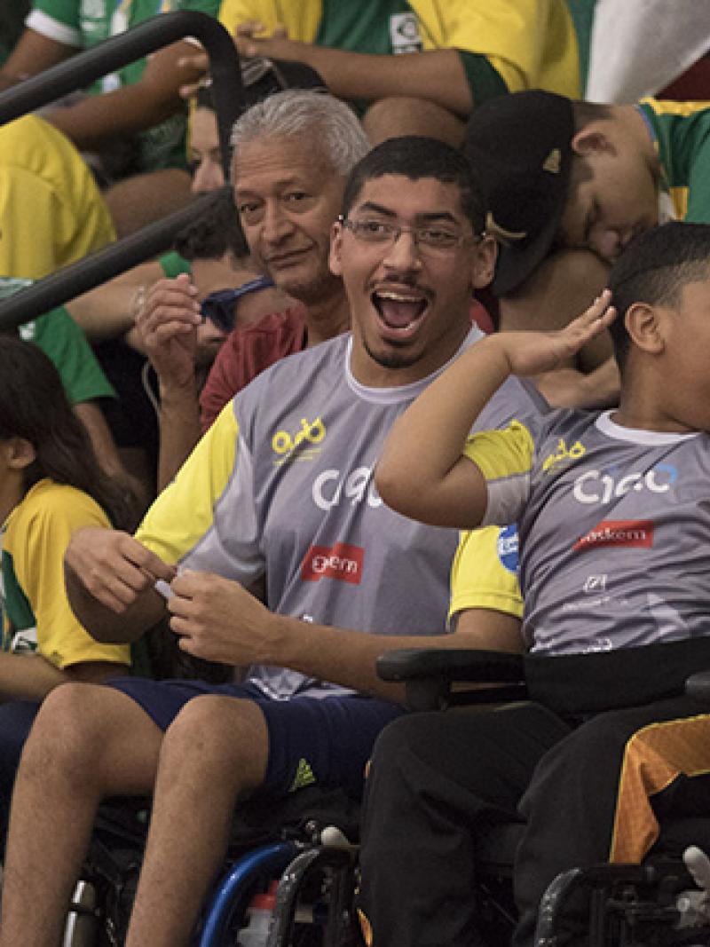 A man and a boy in a wheelchair watch a wheelchair basketball competition