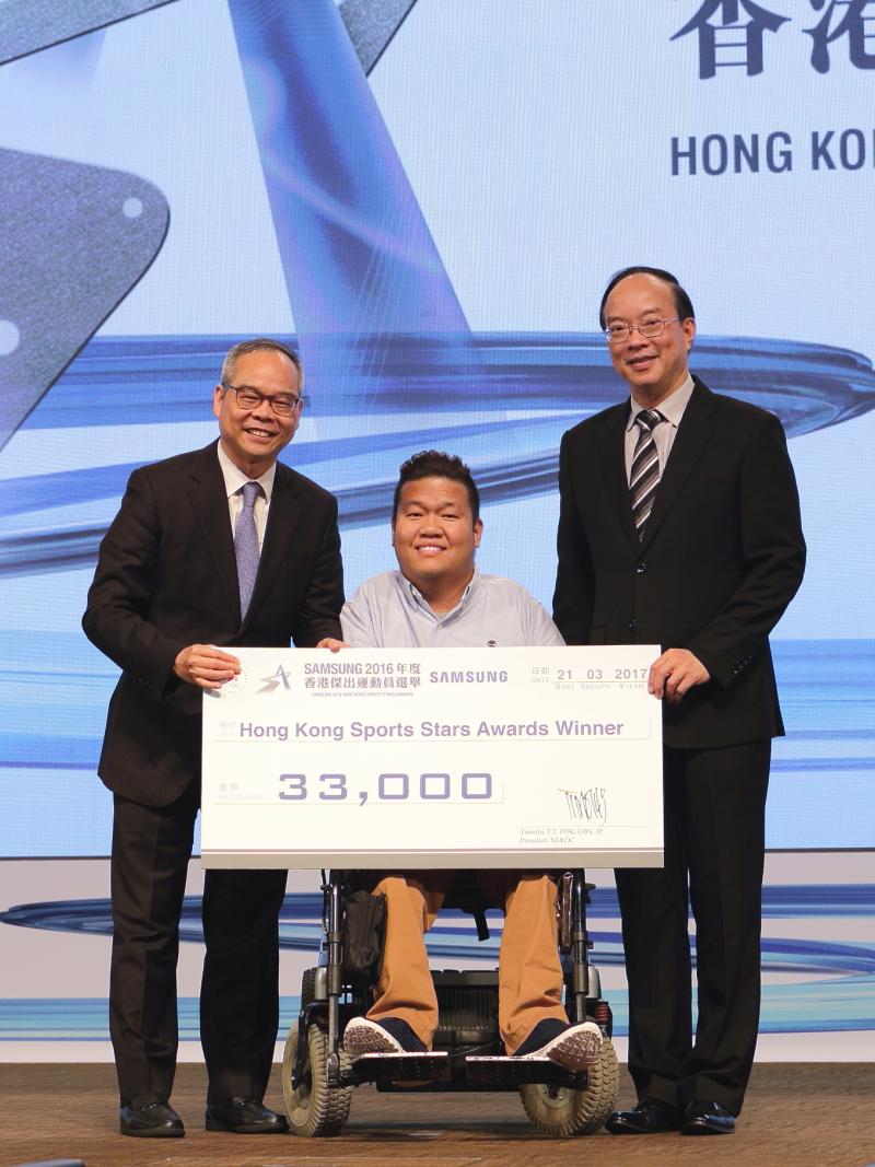 Man in middle in wheelchair holds giant check with two other men standing