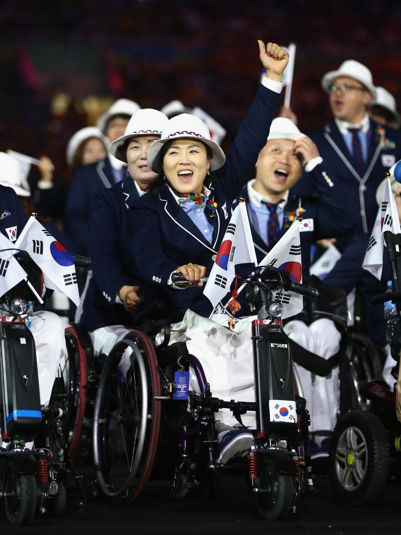 South Korean athletes in wheelchairs hold flags as they enter the stadium