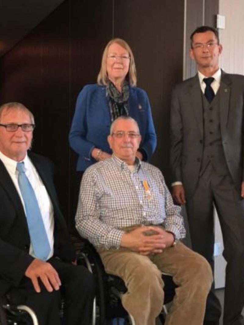 Two men in wheelchairs in suits while two people stand behind them to pose for a photo