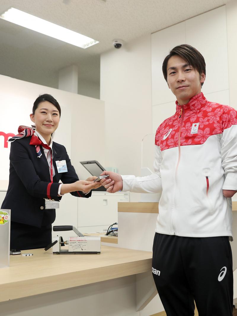 Two Japanese men pose for a photo as a woman hands over a cell phone