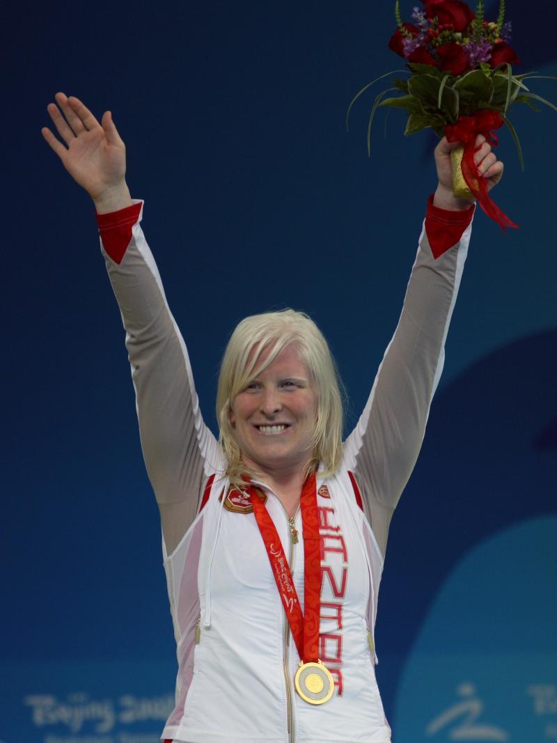 Swimmer raises her arms on the podium to celebrate her medal
