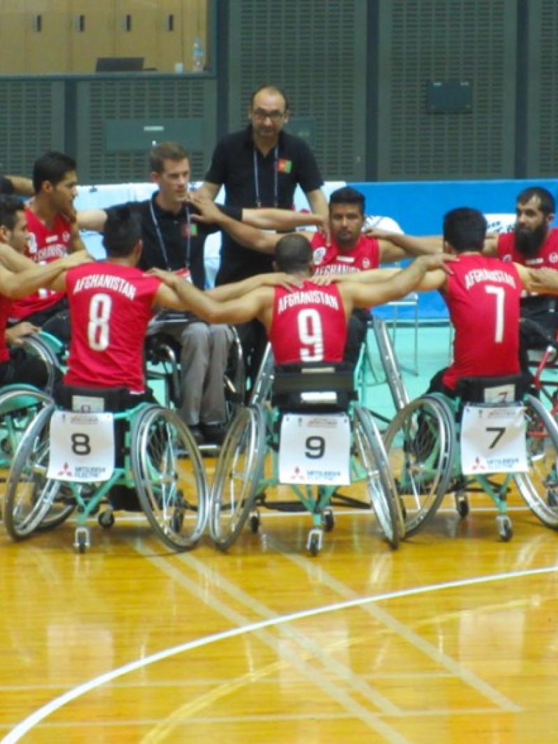 Men in basketball wheelchairs huddle around each other