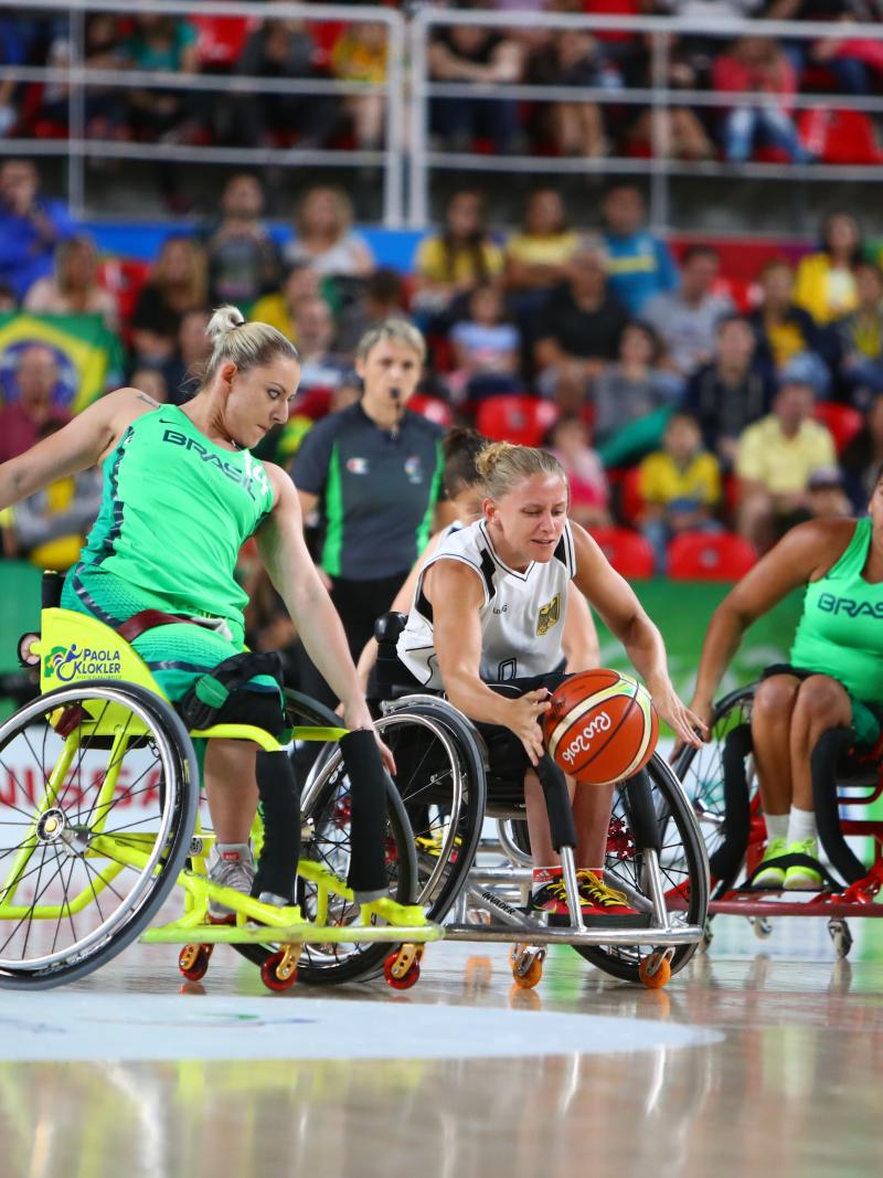 Woman in wheelchair goes for loose basketball while oppents guard her