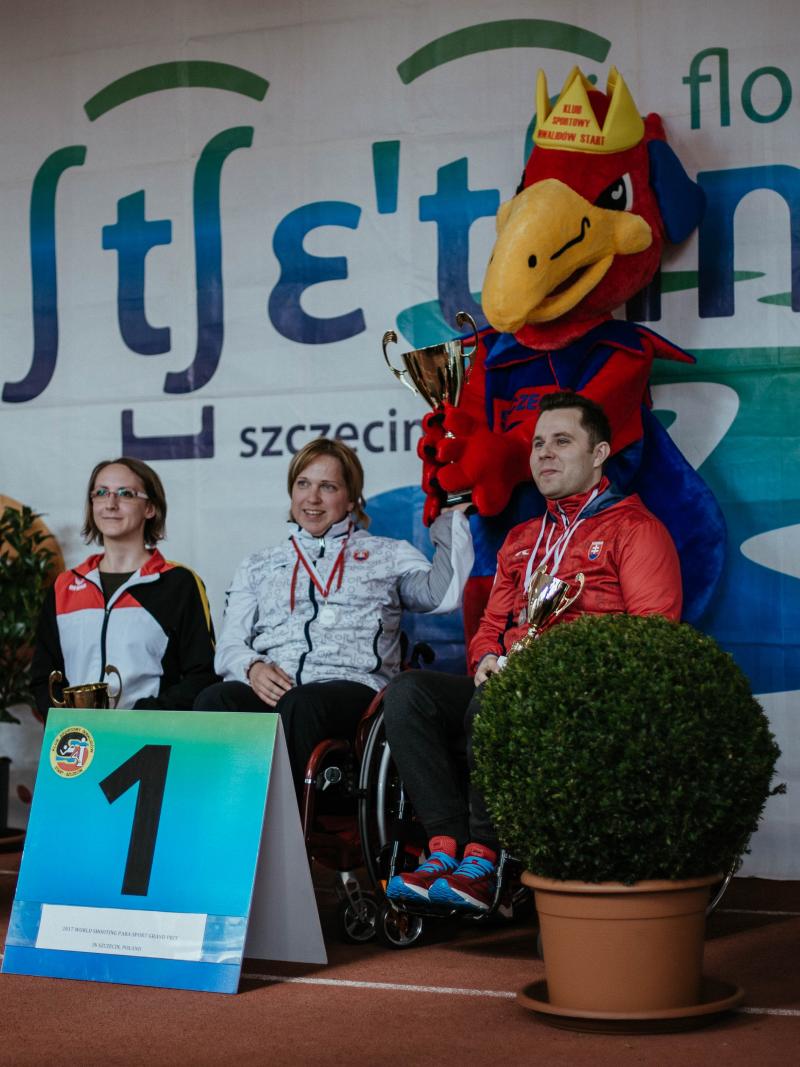 Three shooters on a podium with event mascot