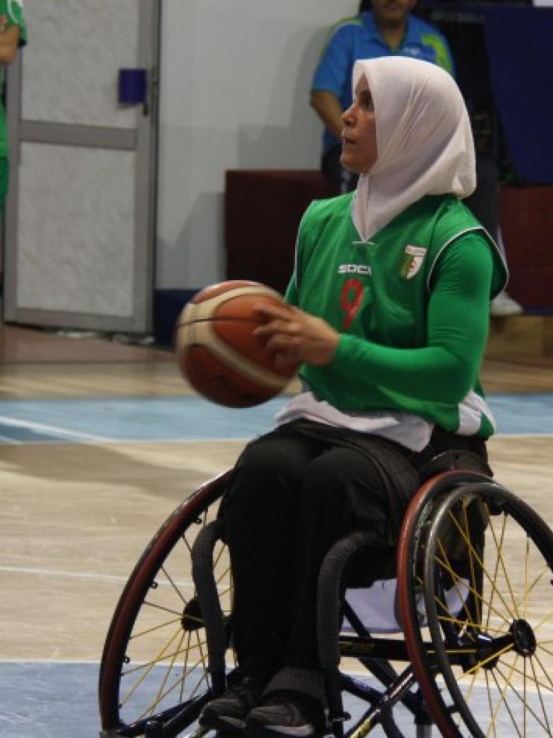 Woman wearing a hijab shooting a basketball in a wheelchair