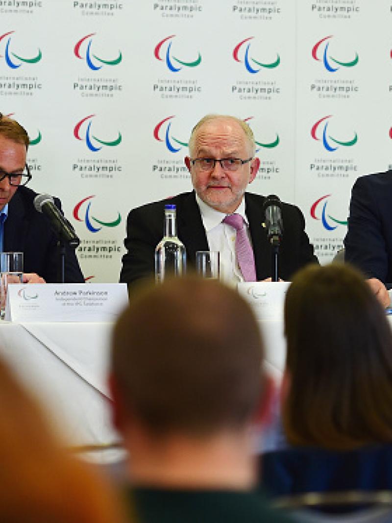 Three men sit at podium during press conference