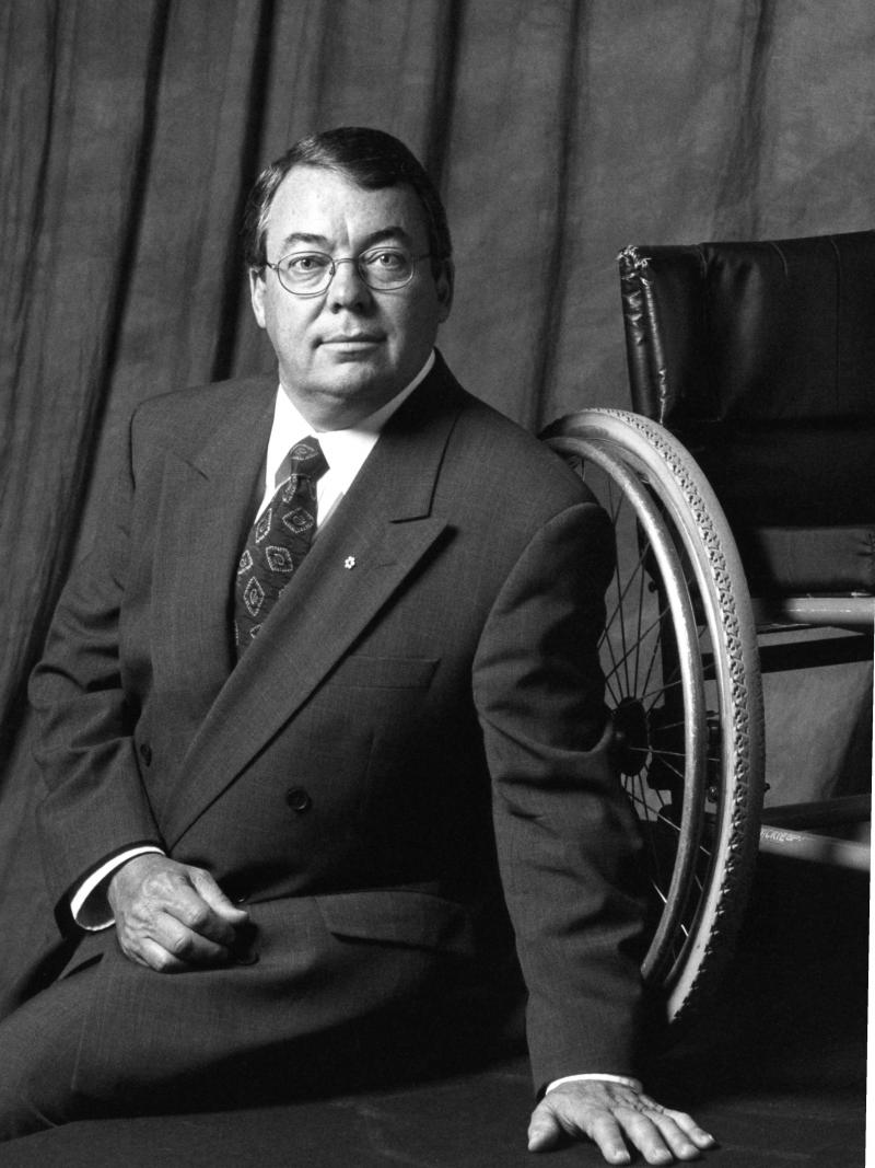 Black and white portrait of a man sitting infront of a wheelchair 