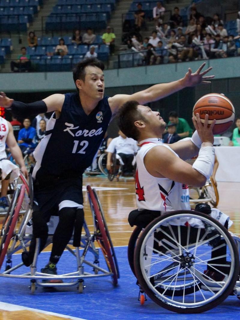 Man in wheelchair tries to block another man in wheelchair playing basketball
