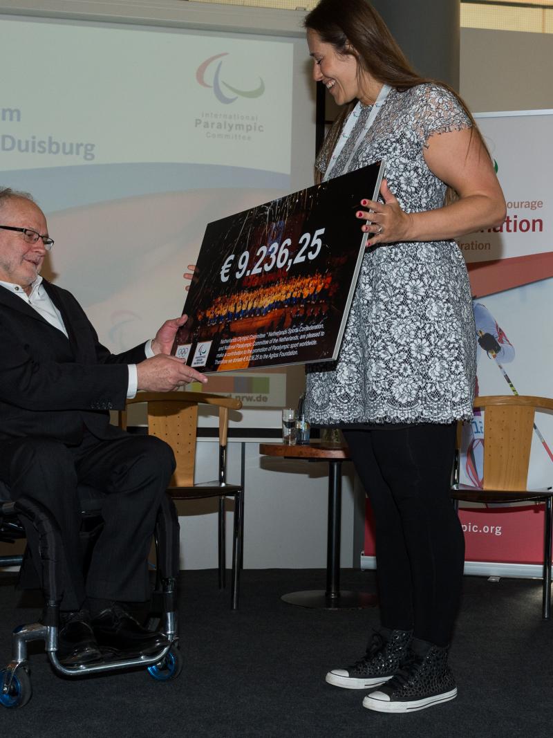 Woman presents man in wheelchair with a cheque