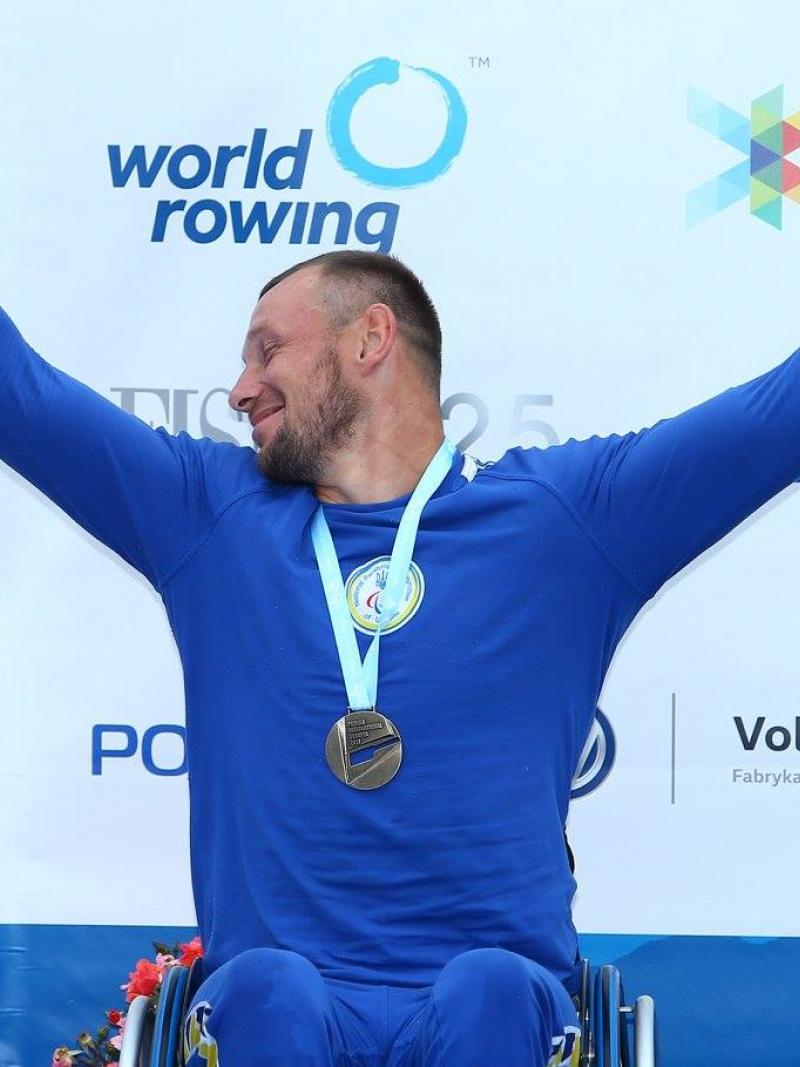 rower raises arms to celebrate gold medal on podium