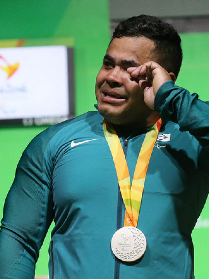 man cries while holding silver medal on podium