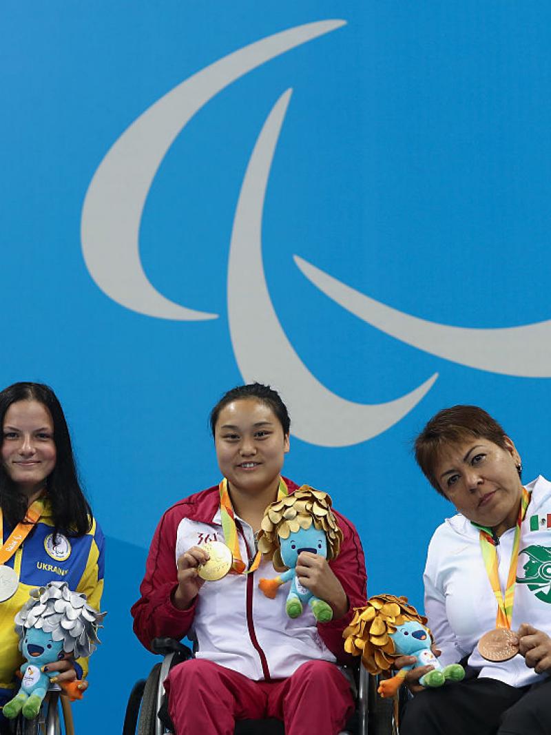 three women in wheelchairs holding medals on a podium