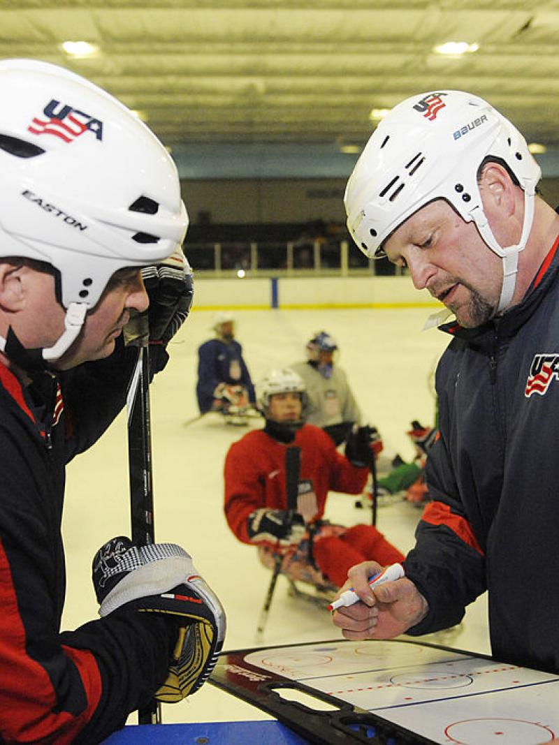 two men discuss ice hockey tactics on a tactics board