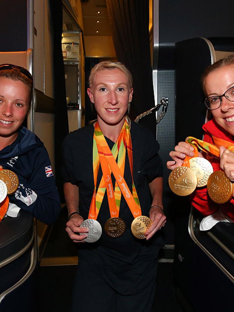 three women on a plane holding their Paralympic medals and smiling