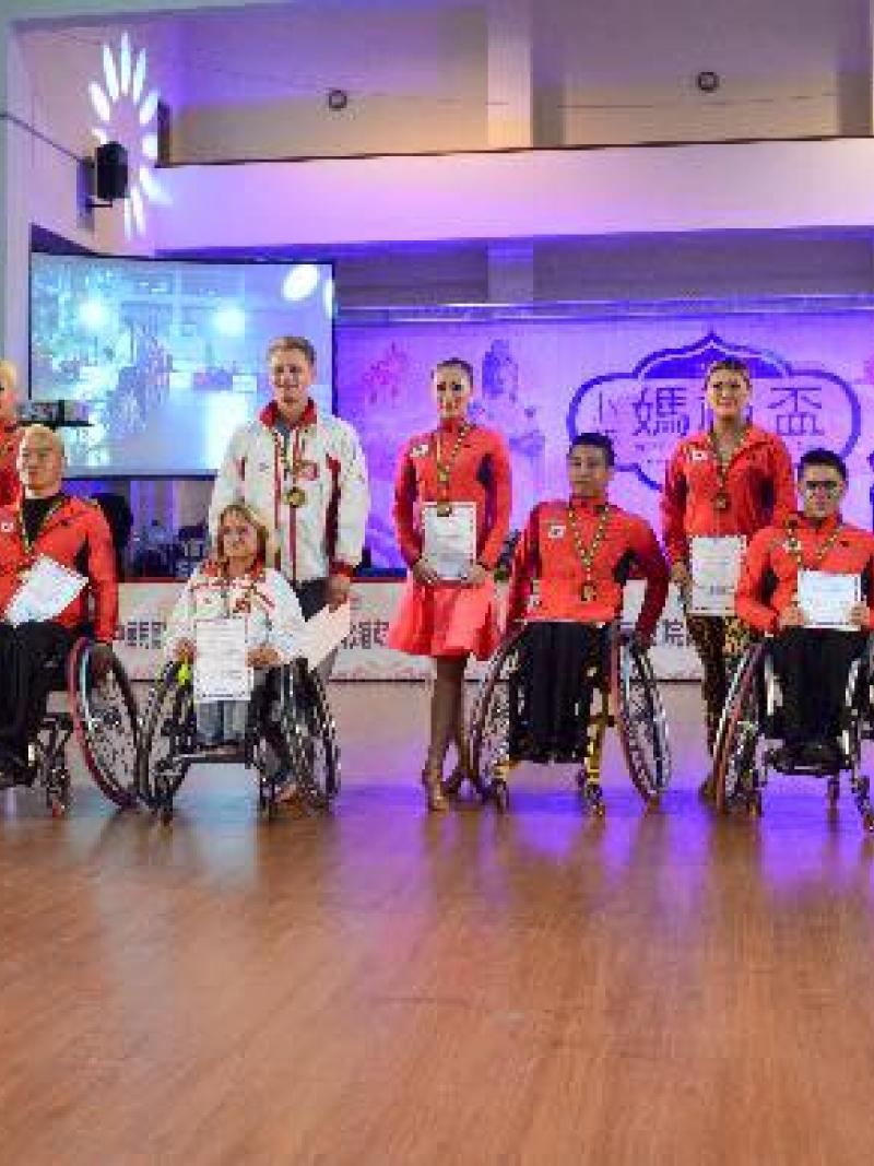 A row of men and women in wheelchairs with competition certificates