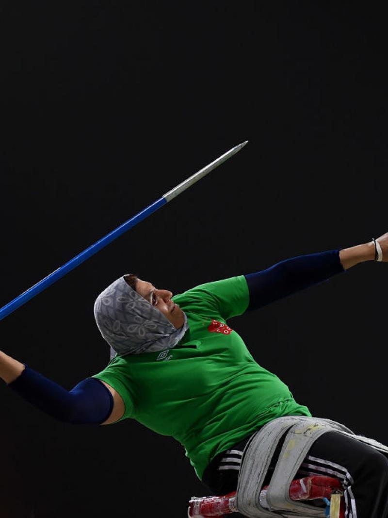 woman in a wheelchair leans back to throw a javelin