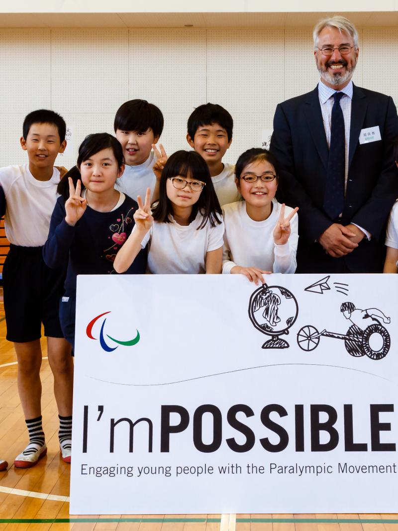 a group of children and a man smile for the camera holding a sign