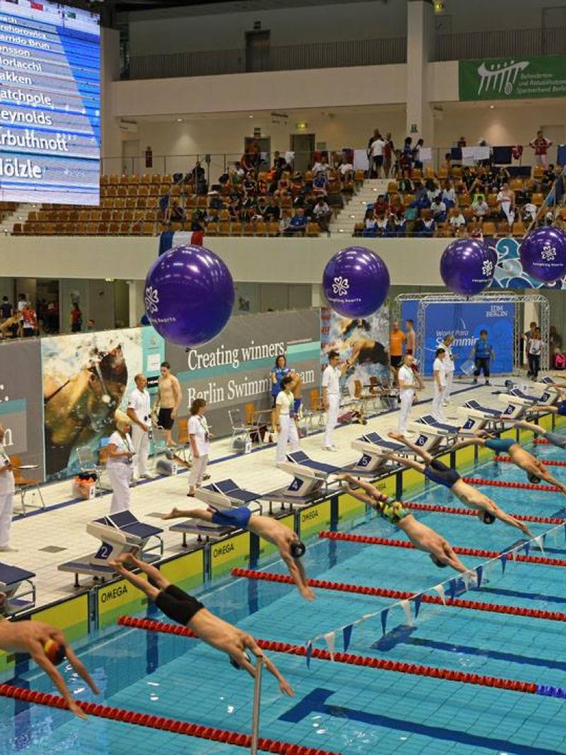 a group of male para swimmers dive into the pool
