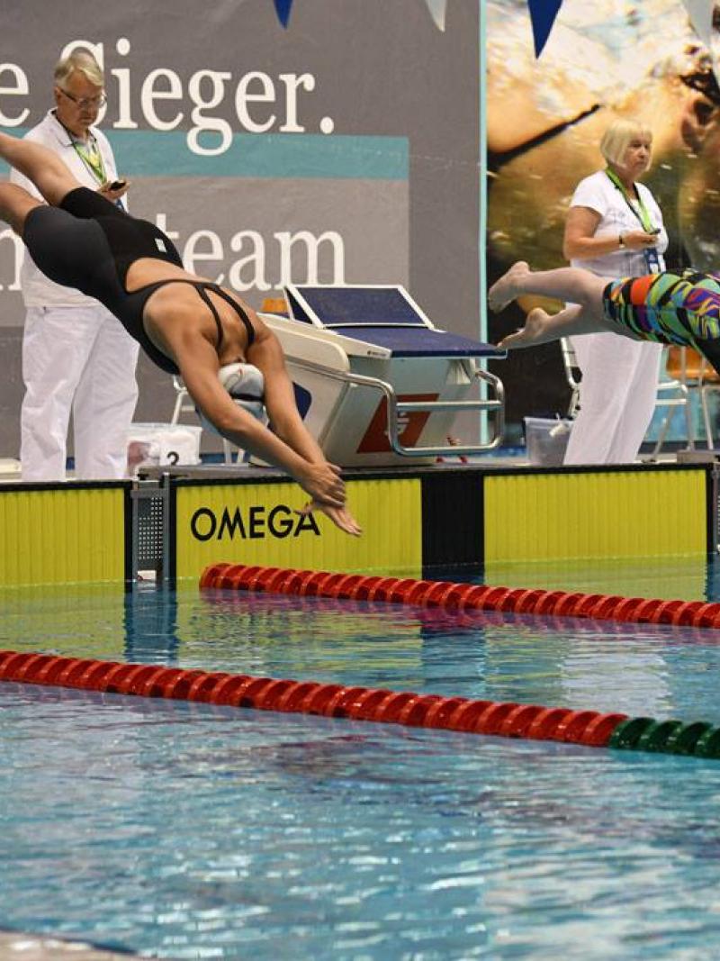 two female swimmers jump into the pool at the start of a race