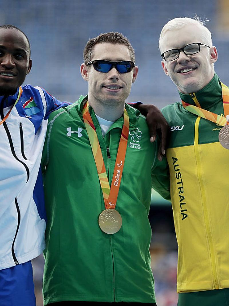 three men stand on a podium with their medals