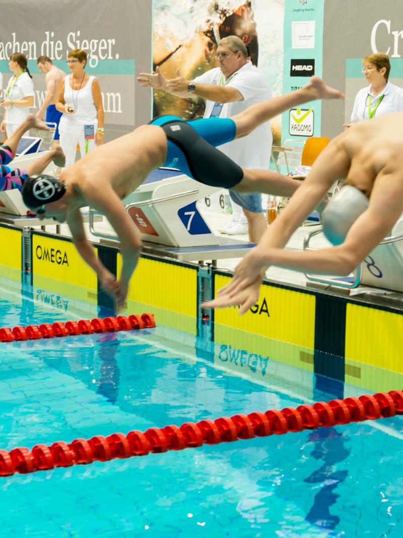 a group of male swimmers dive into the pool at the start of the race
