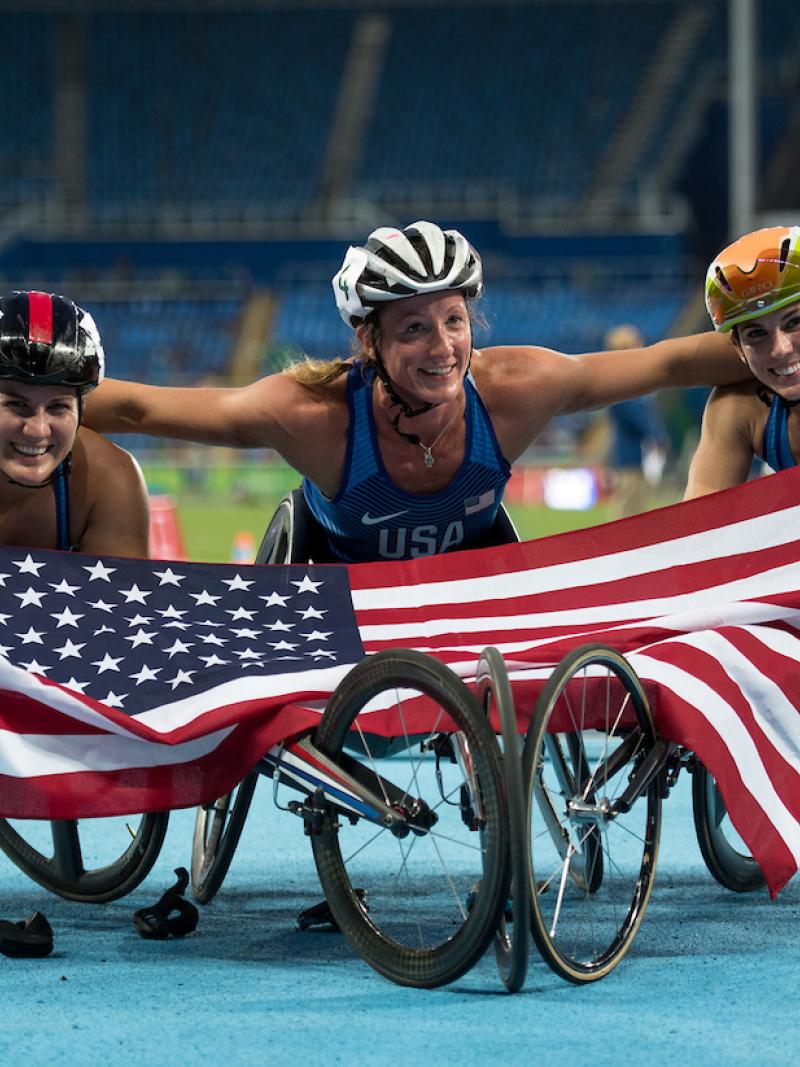 three female wheelchair athletes hold up the American flag