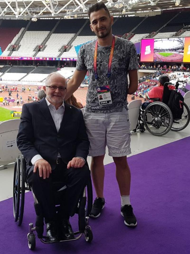 a para athlete stands beside a man in a wheelchair