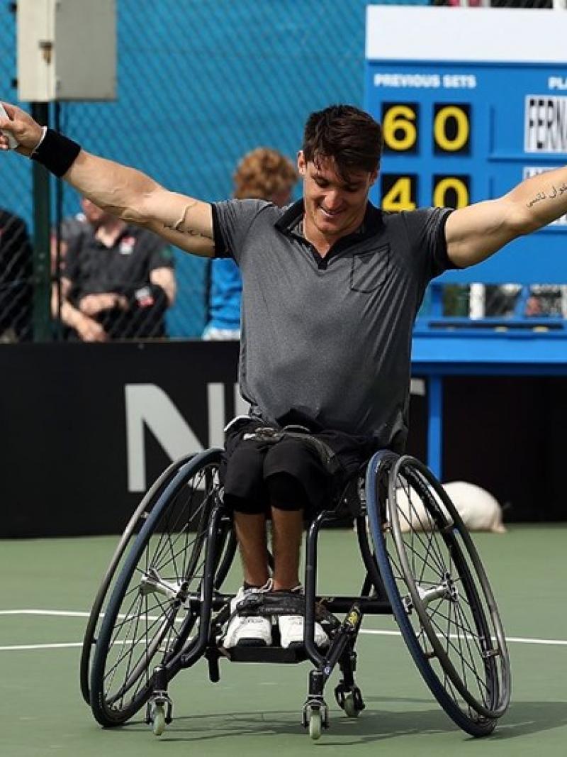 a wheelchair tennis player raises his arms in celebration