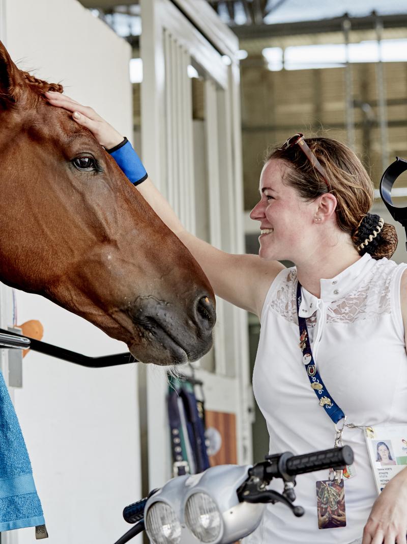 a para equestrian rider pats her horse in the stables