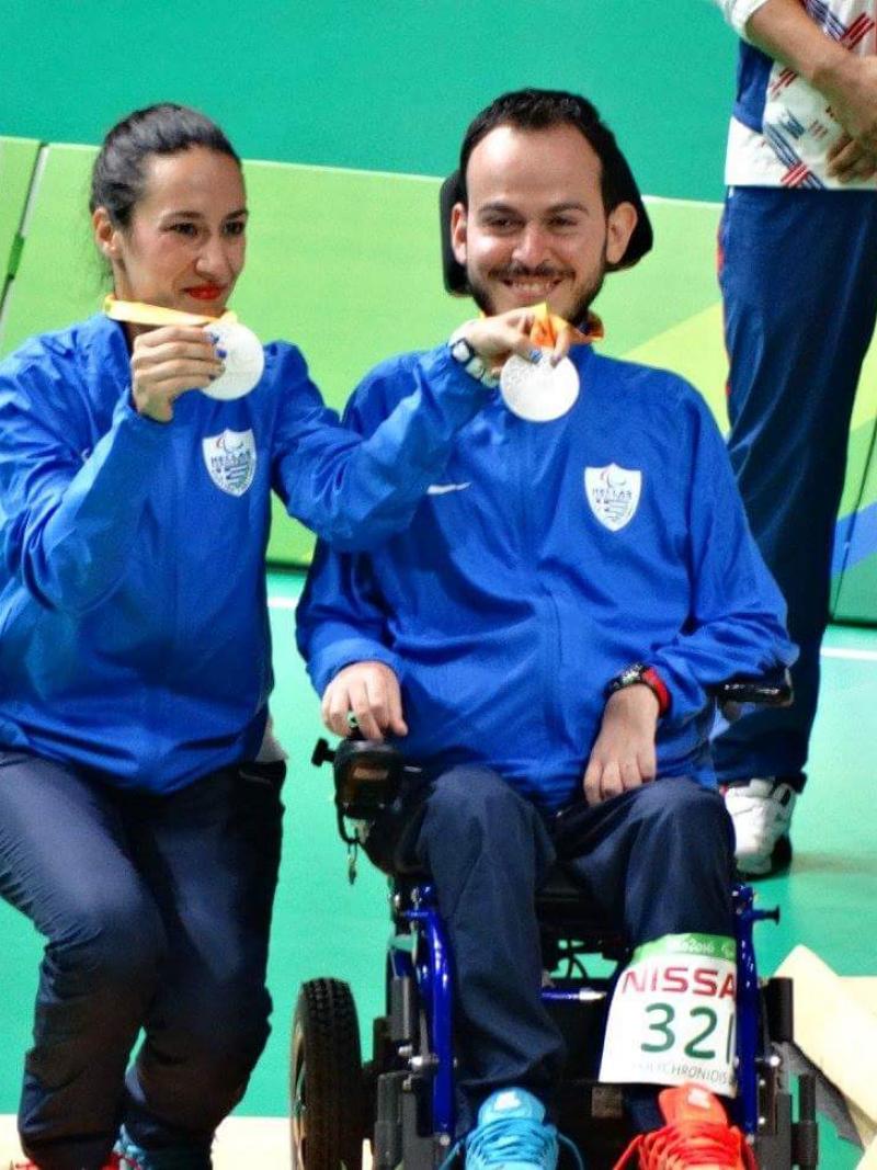 a woman and a man in a wheelchair hold up their silver Paralympic medals