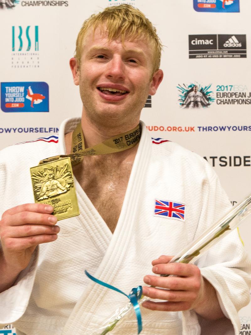 a man holds up his gold medal and smiles