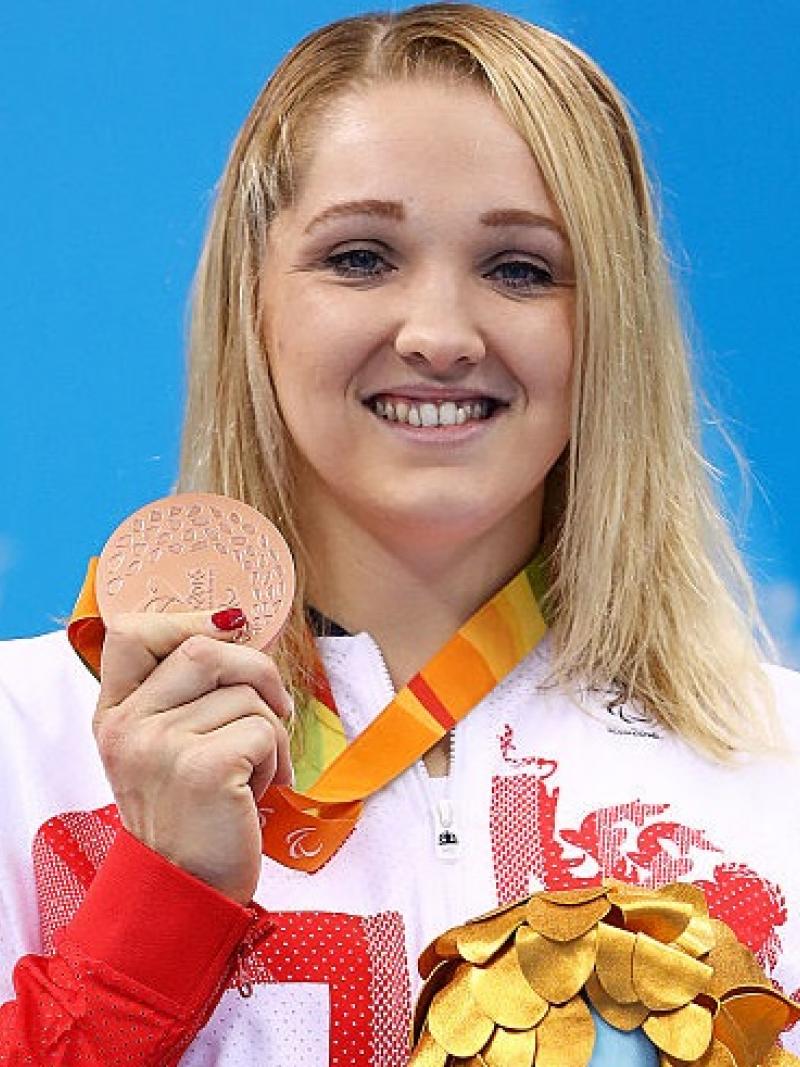 a woman holds up her medal and her mascot