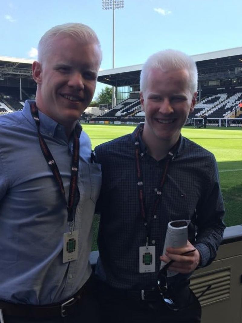 two men smile at the side of a football pitch