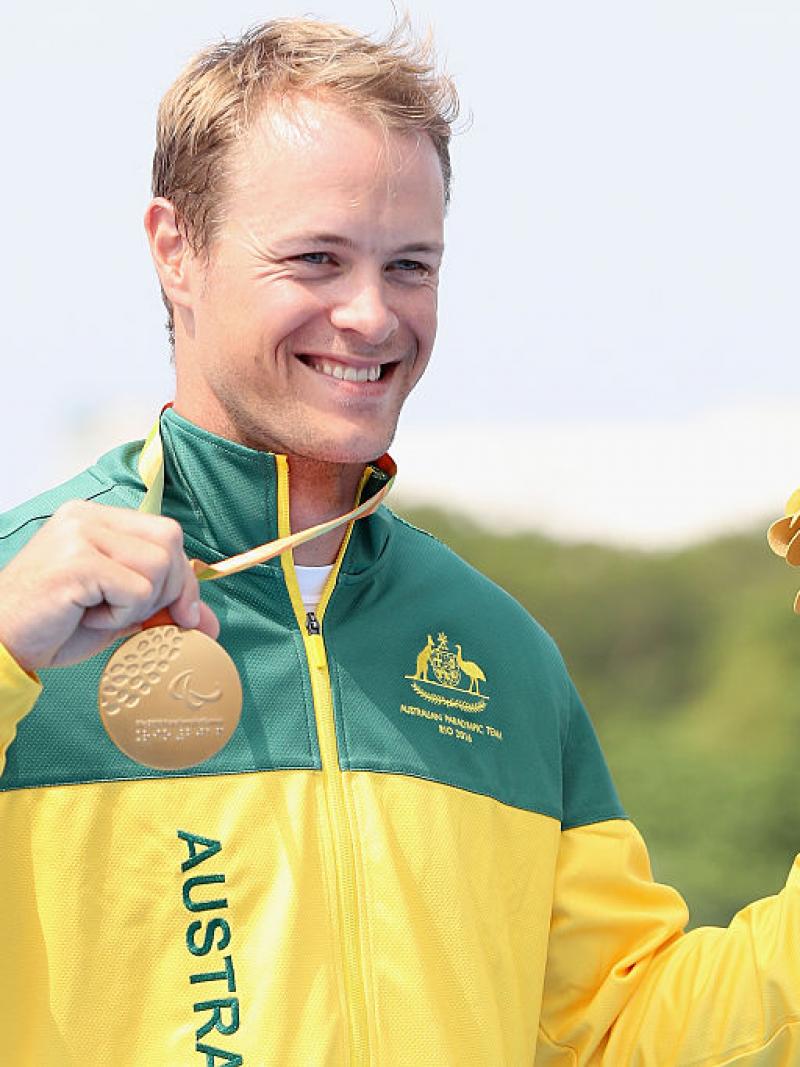 a man holds up his gold medal on the podium