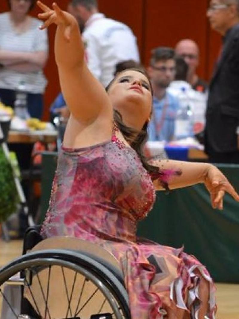 a para dancer in a wheelchair raises her arms