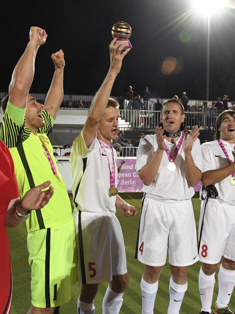 a group of male blind footballers raise their arms in celebration