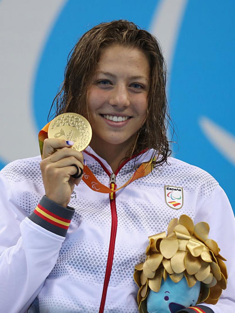 a female Para swimmer holds up her gold medal