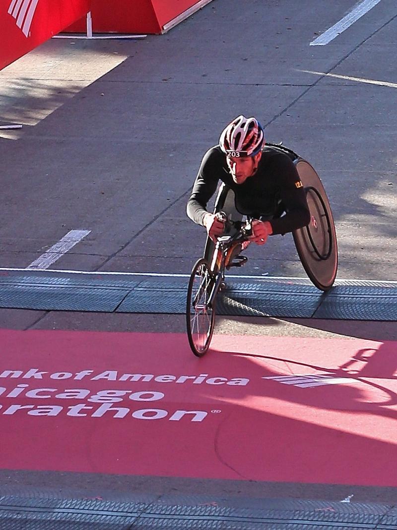 a male wheelchair racer crosses the finish line