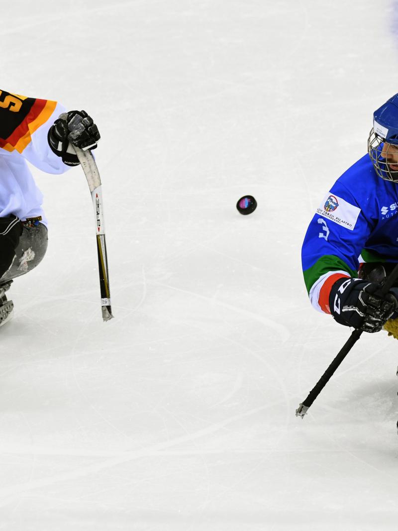 two male Para ice hockey players contest a puck