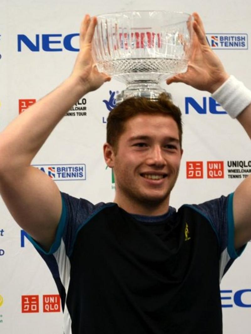 A male wheelchair tennis player lifts a glass trophy