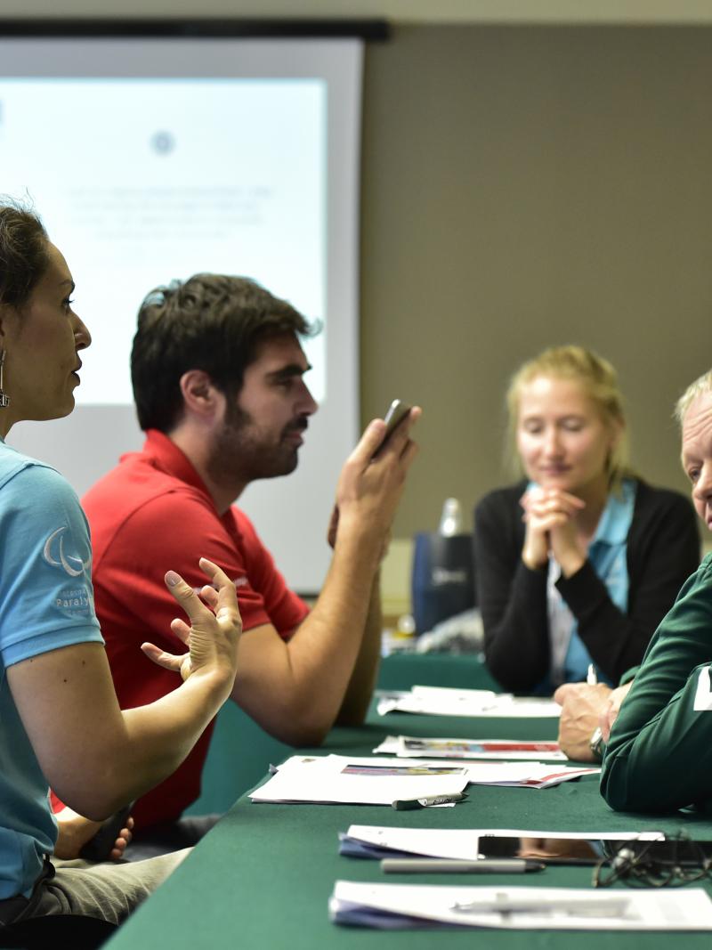 Four people talking in a meeting with a fifth person in the background