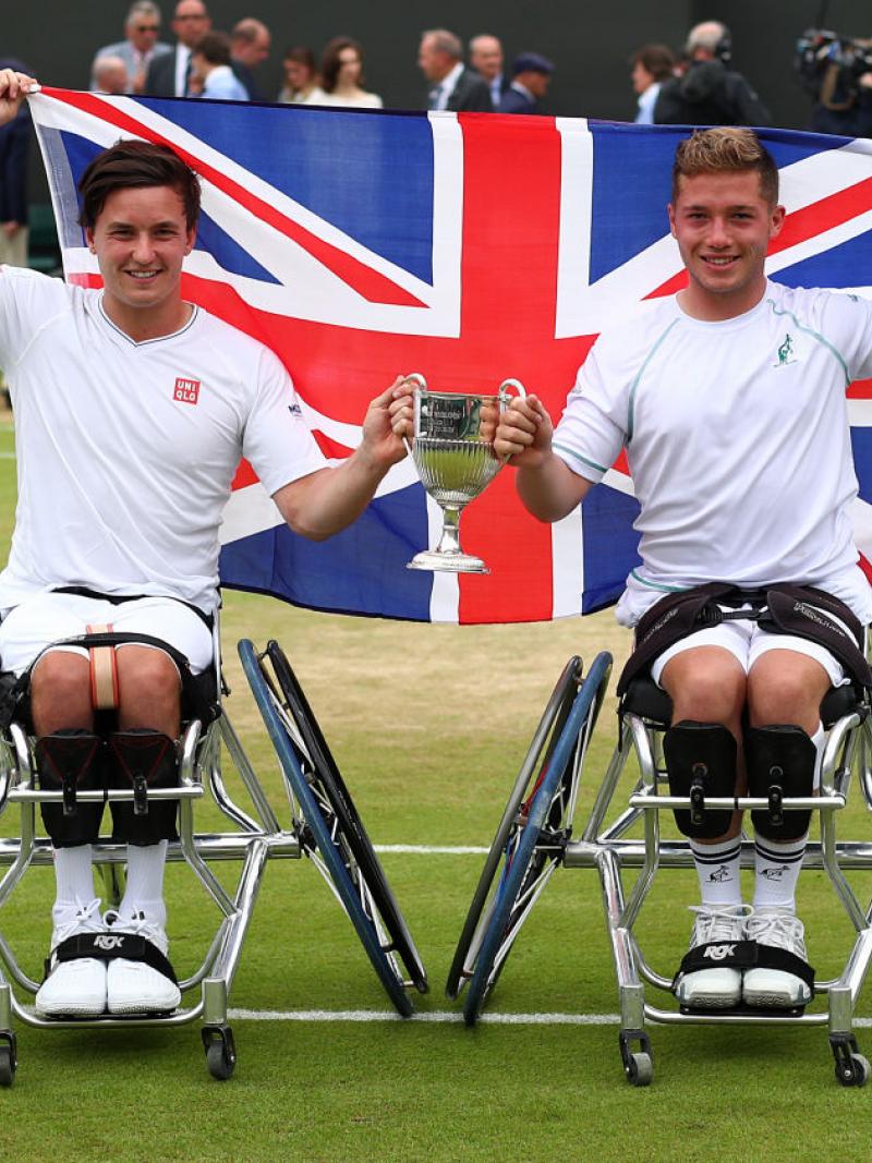 two male wheelchair tennis players hold their trophy and the British flag