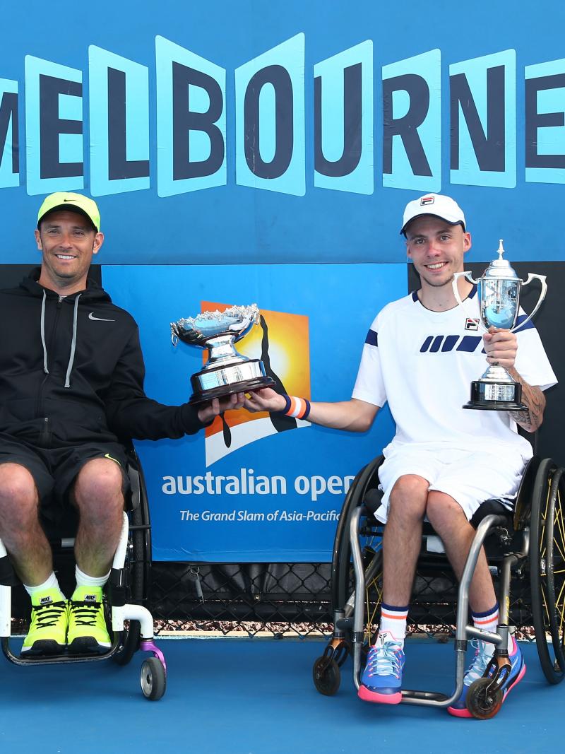 two male wheelchari tennis players hold up a trophy between them