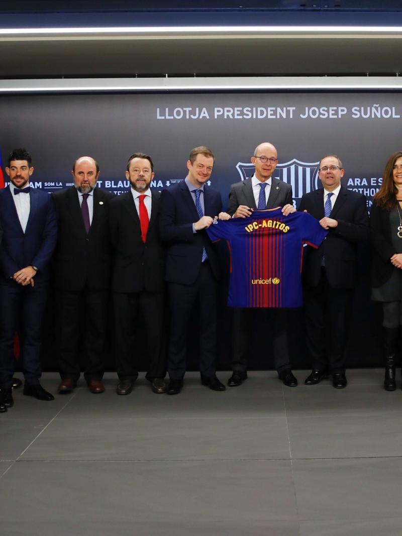 a group of men and women stand holding a Barcelona shirt
