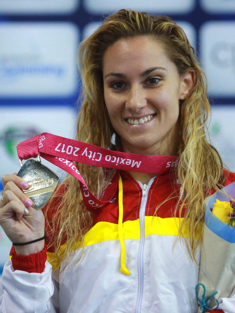 a female Para swimmer holds up her gold medal on the podium