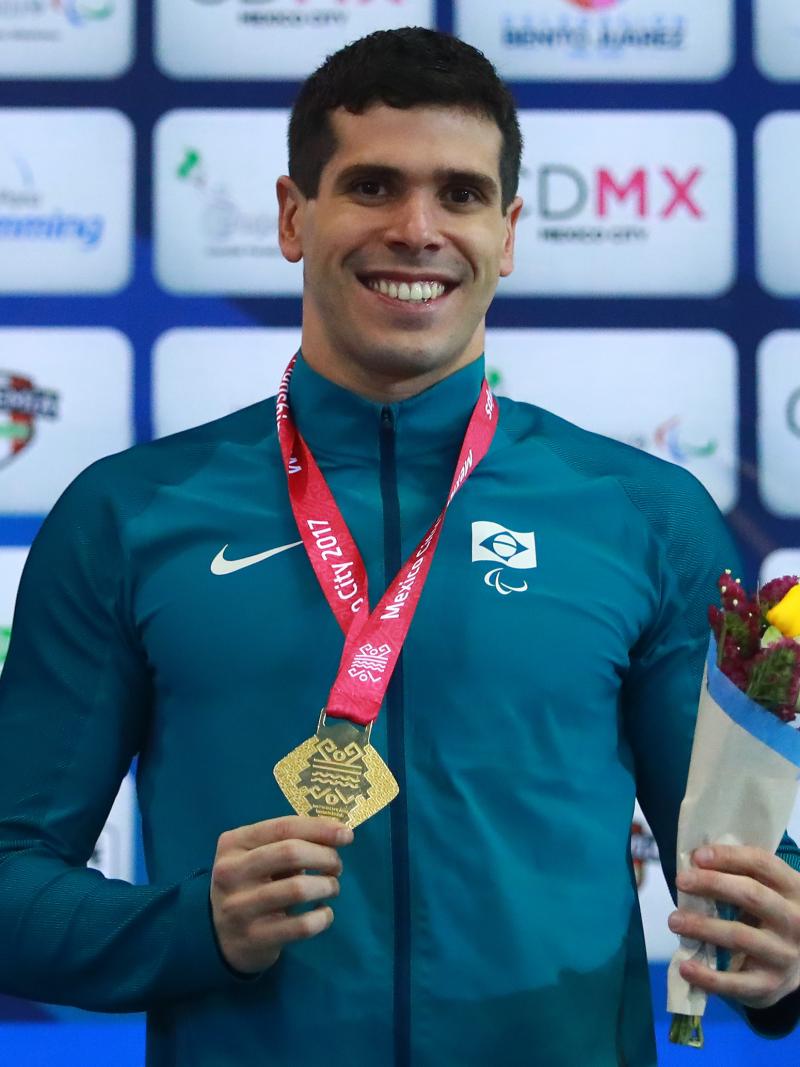 A male Para swimmer smiles holding his gold medal