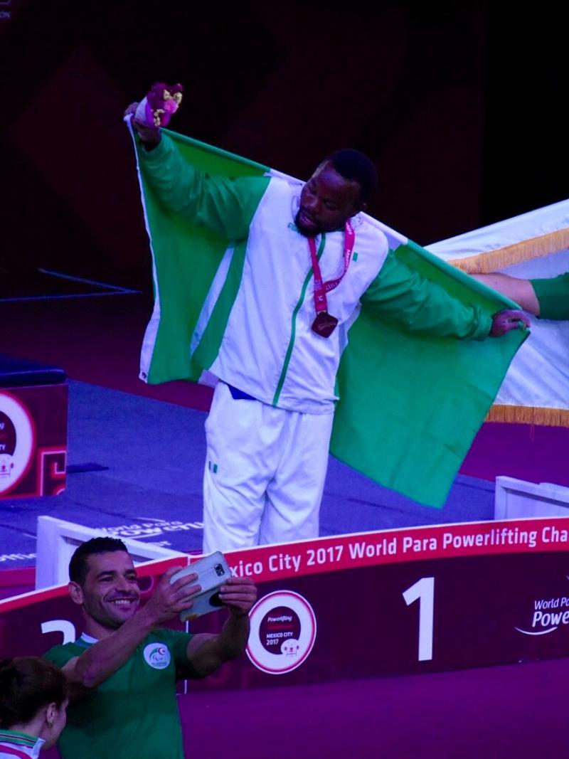 three powerlifters on the podium, two holding up flags