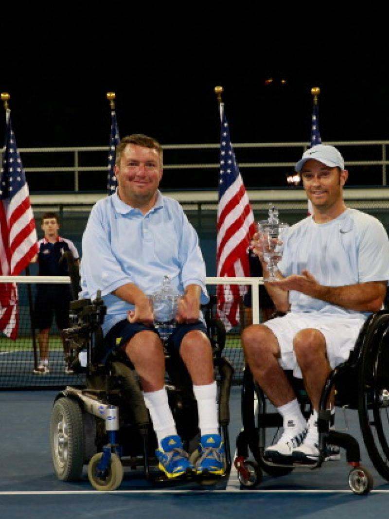 Two men in wheelchairs pose for photo on tennis court